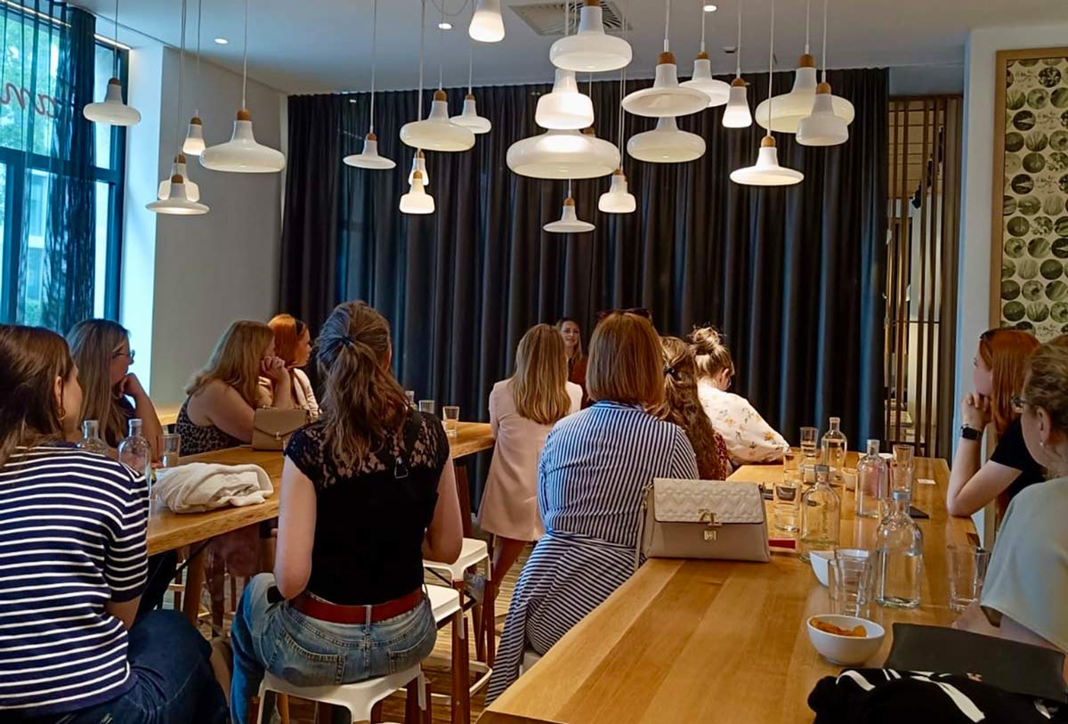 Mehrere Frauen sitzen aufmerksam an einem langen Holztisch in einem sonnigen Raum